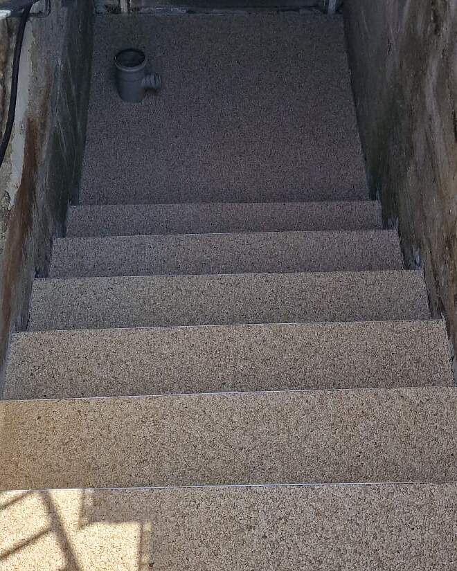 Fertig beschichteter Kellerabgang: Außentreppe mit fugenlosem Steinteppich in Beige- und Grautönen, wasserdurchlässig und rutschhemmend.