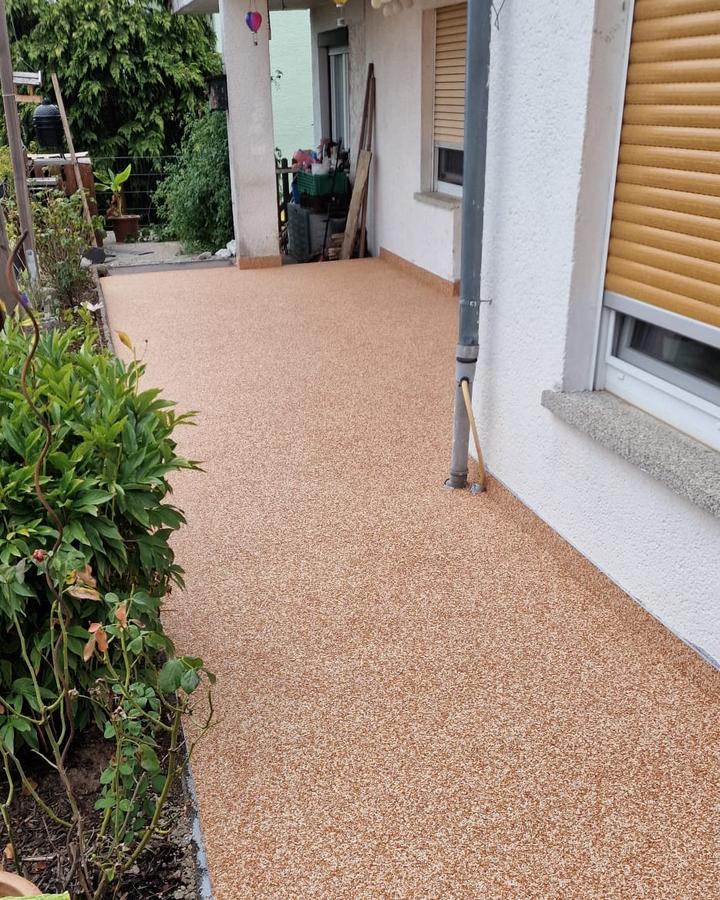 Hauszugang mit Steinteppich in Terracotta: durchgehende Fläche entlang der Hauswand, sauber an Fallrohr und Beetkante angearbeitet.