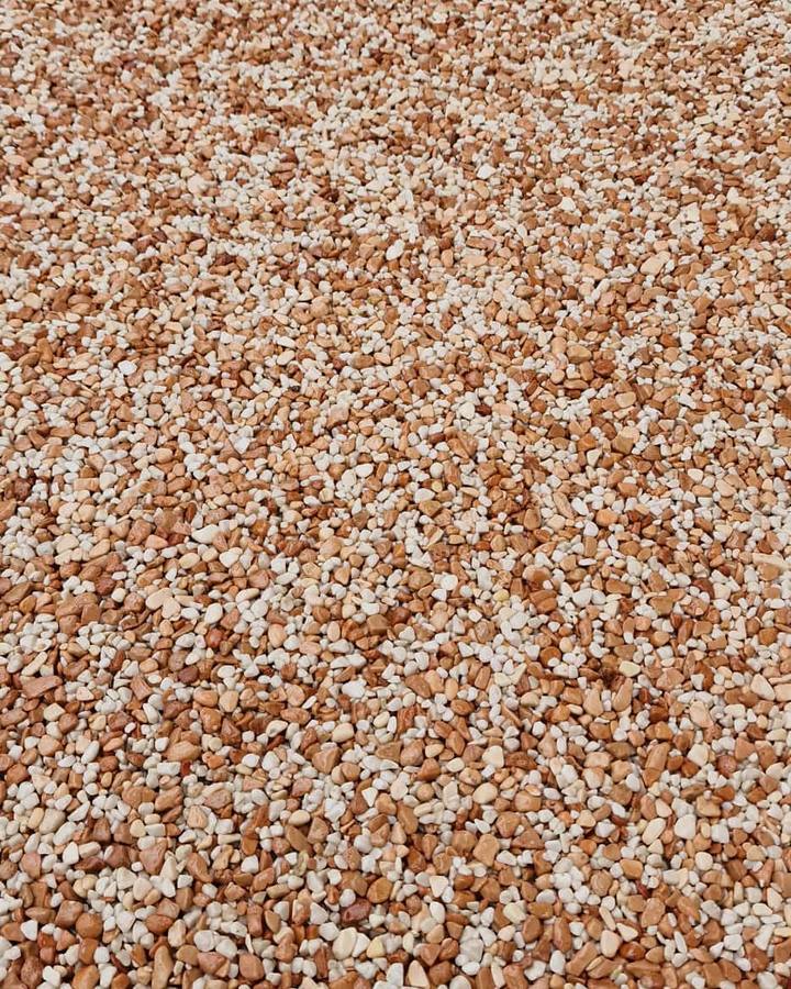Nahaufnahme der Steinteppich-Oberfläche: gerundete Marmorkiesel in Terracotta und Weiß, offenporig und wasserdurchlässig gebunden.
