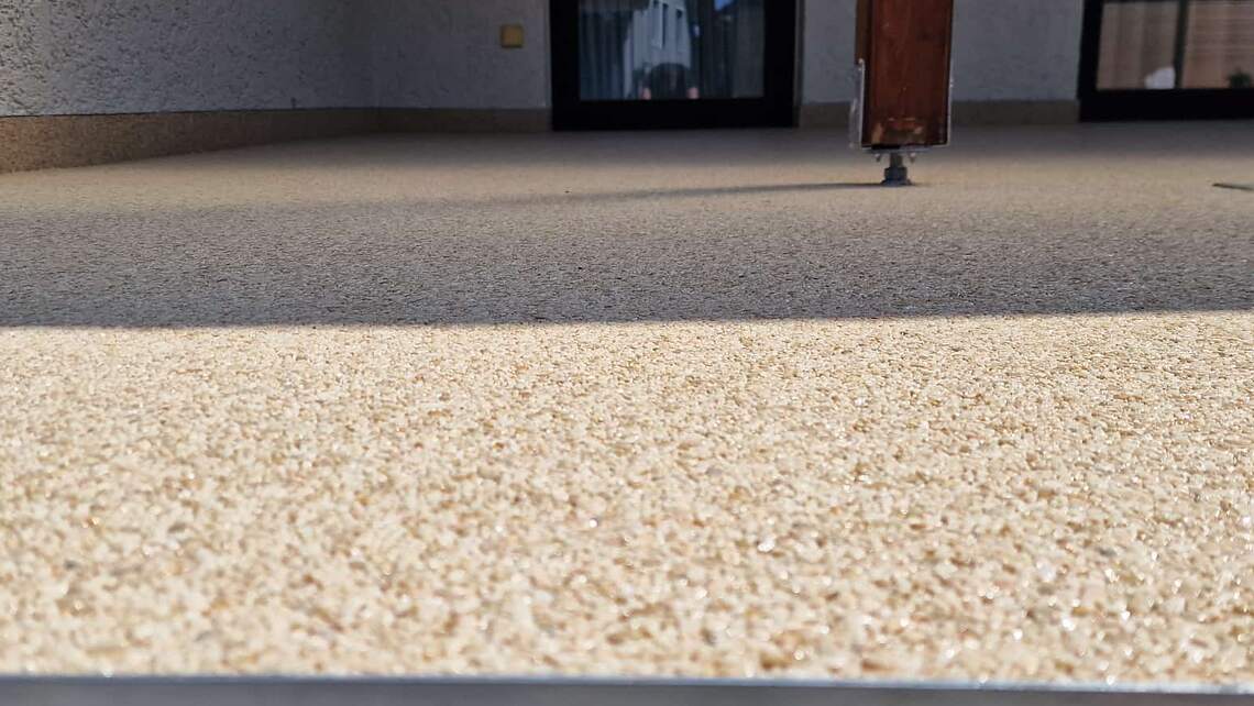 Terrasse mit fugenlosem Steinteppich in Beige vor einem Wohnhaus – durchgehende Fläche ohne Fugen bis an die Terrassentür.
